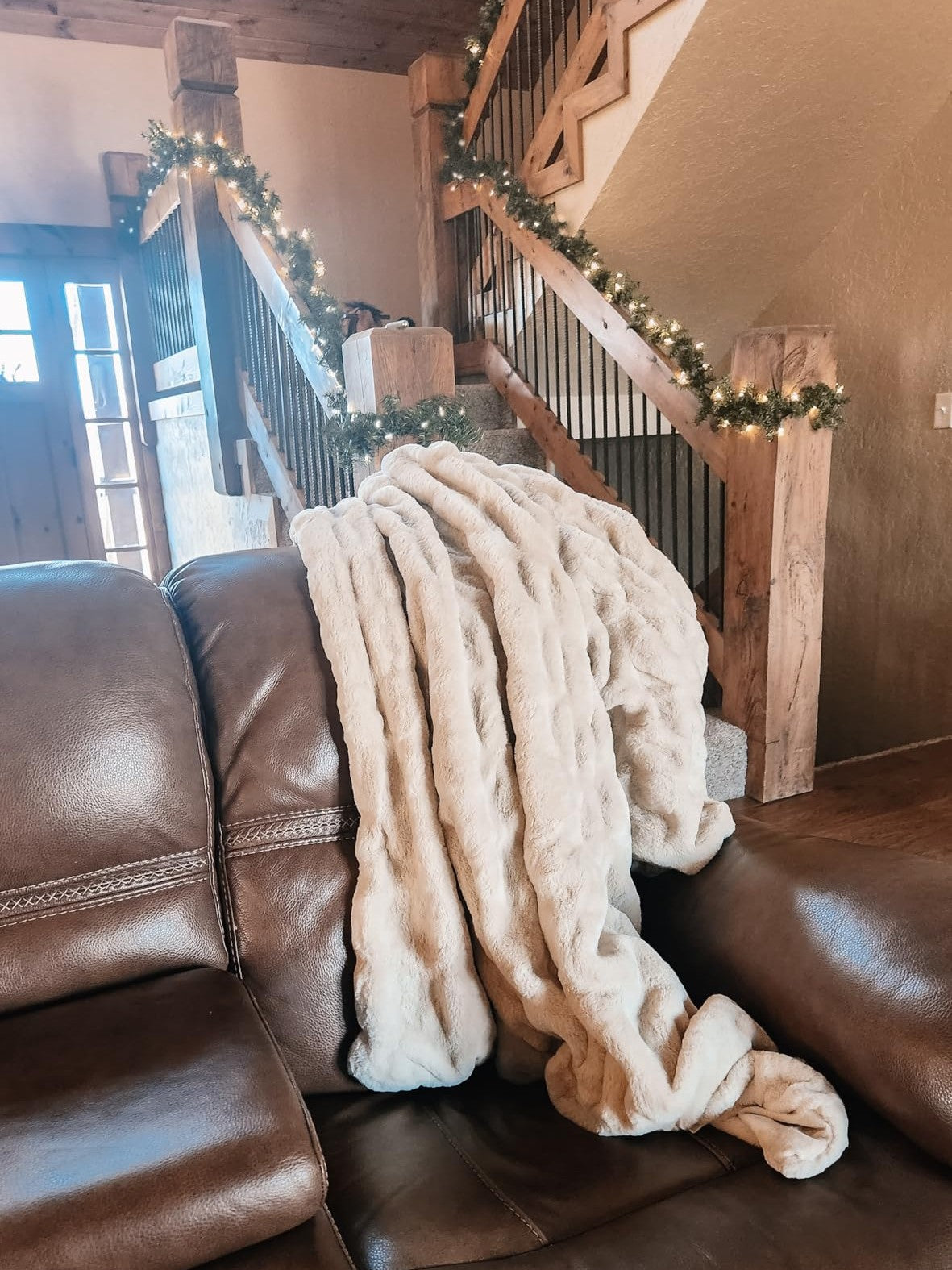 Customer photo showing Aruva SereneWeave throw draped over a brown leather sofa with a staircase and Christmas lights in the background.